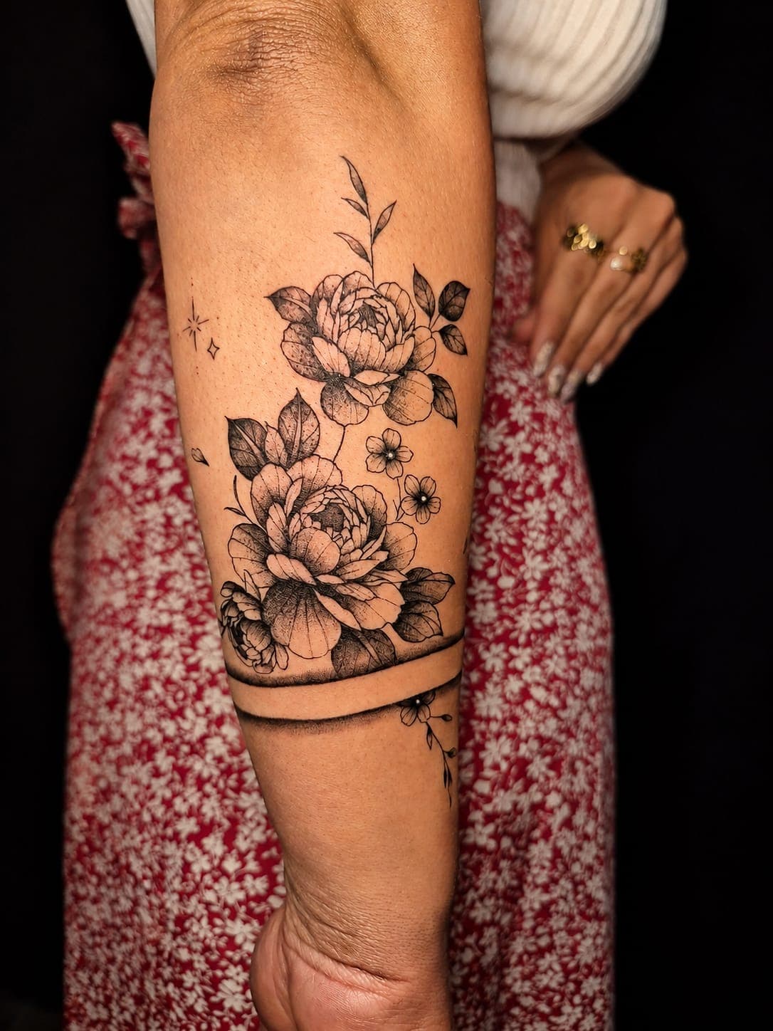 Pivoines tatouées en ligne fine au-dessus d'un bracelet, sur l'avant-bras, à Gruissan