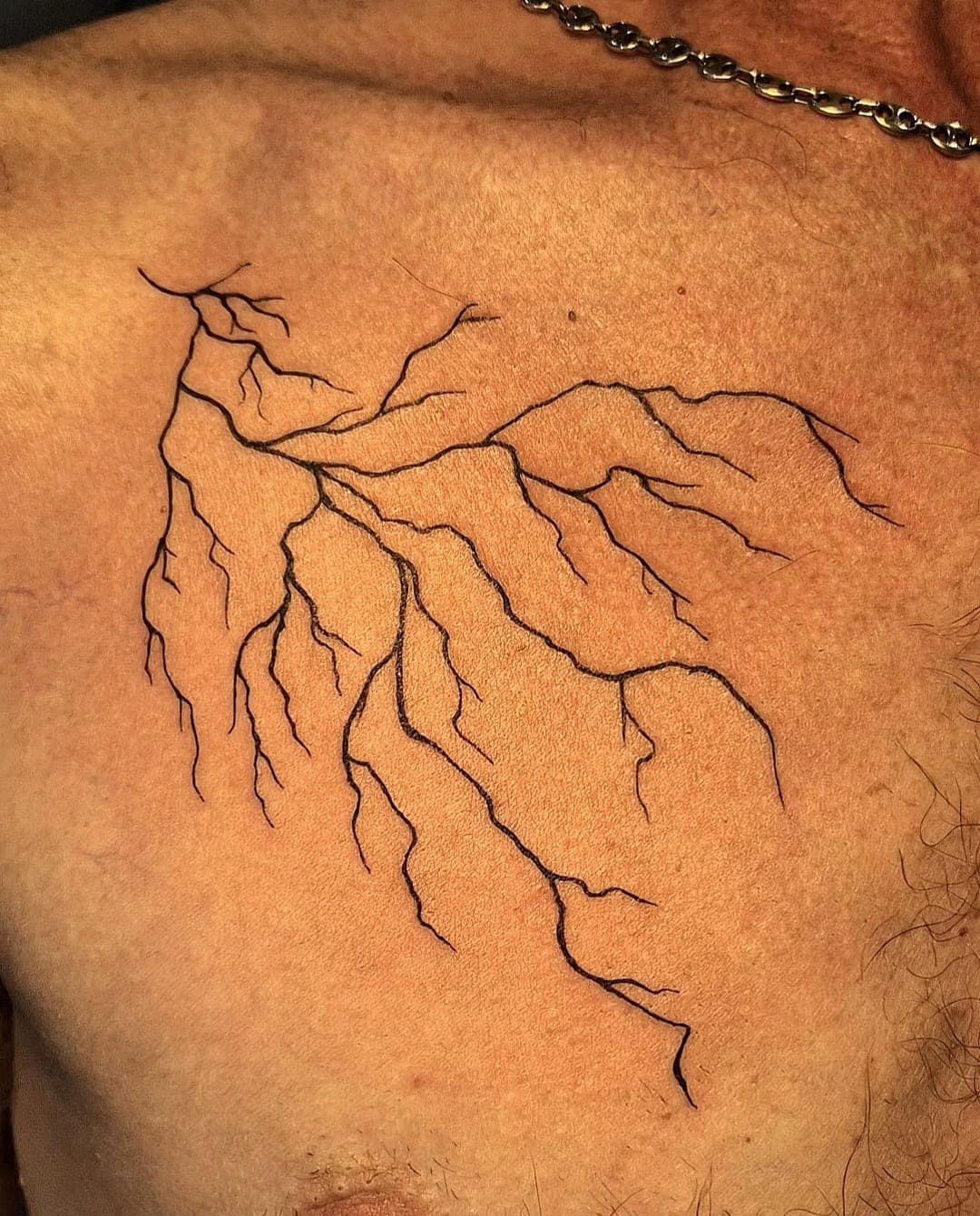 Éclair ramifié tatoué en ligne fine sur le haut du bras, trait unique sans ombrage