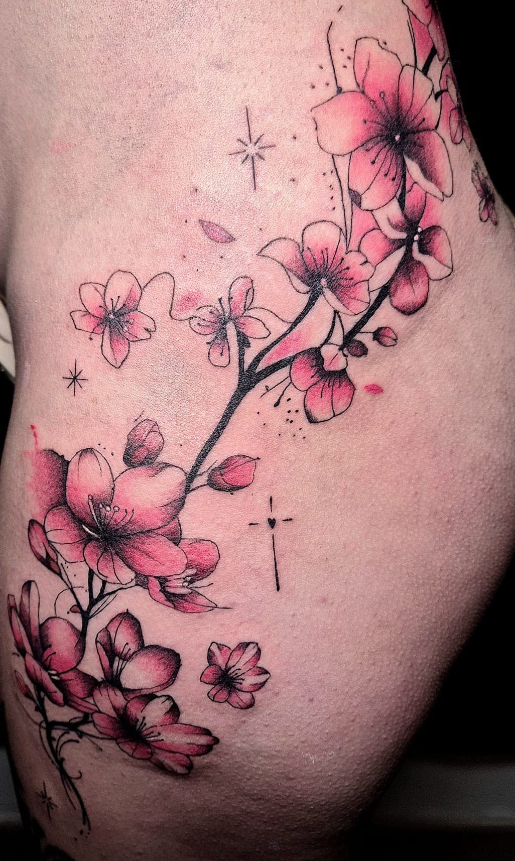 Branche de cerisier en fleurs roses tatouée en ligne fine sur la hanche