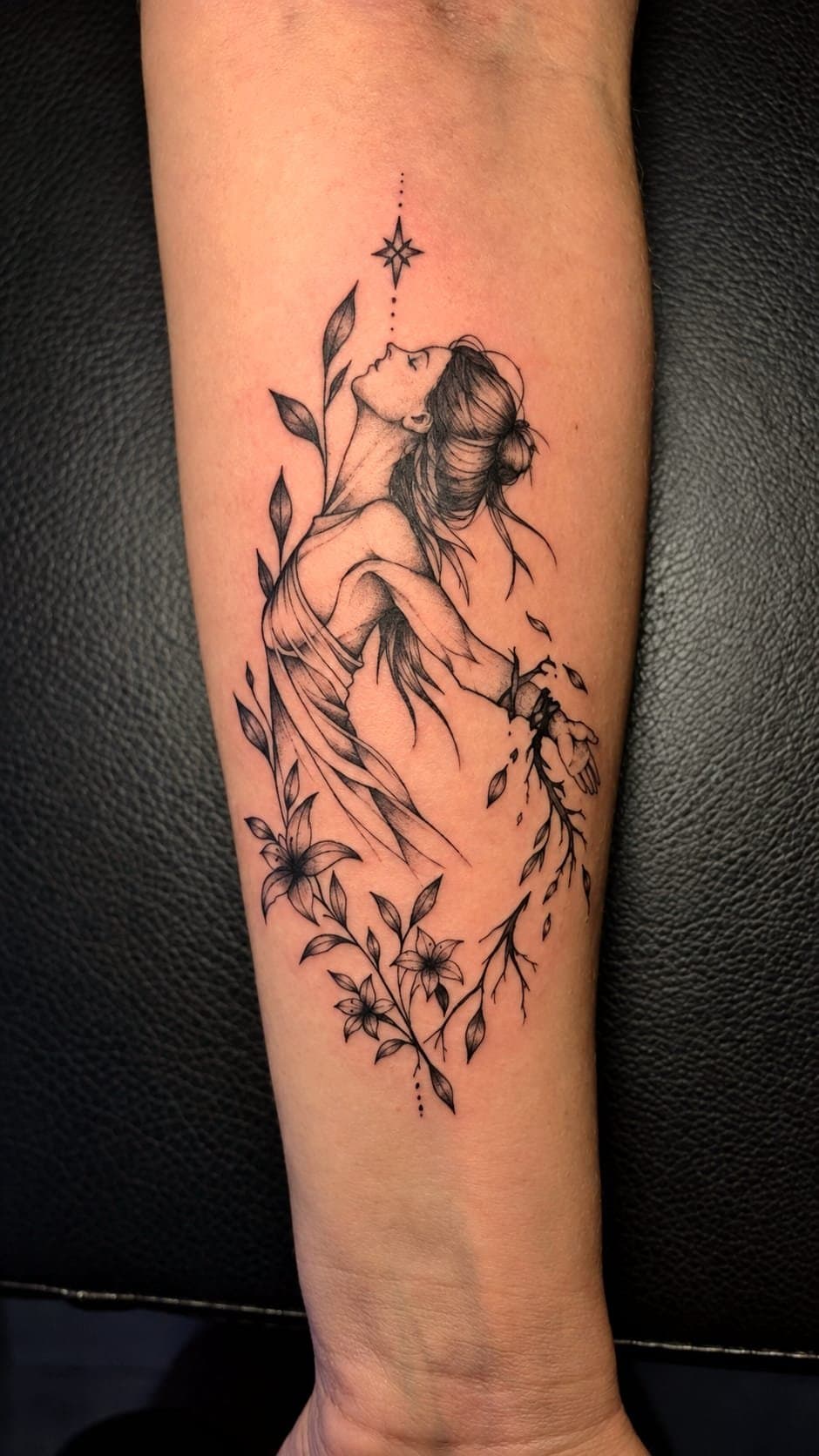 Femme de profil tournée vers une étoile, lys et rameaux tatoués en ligne fine sur l'avant-bras