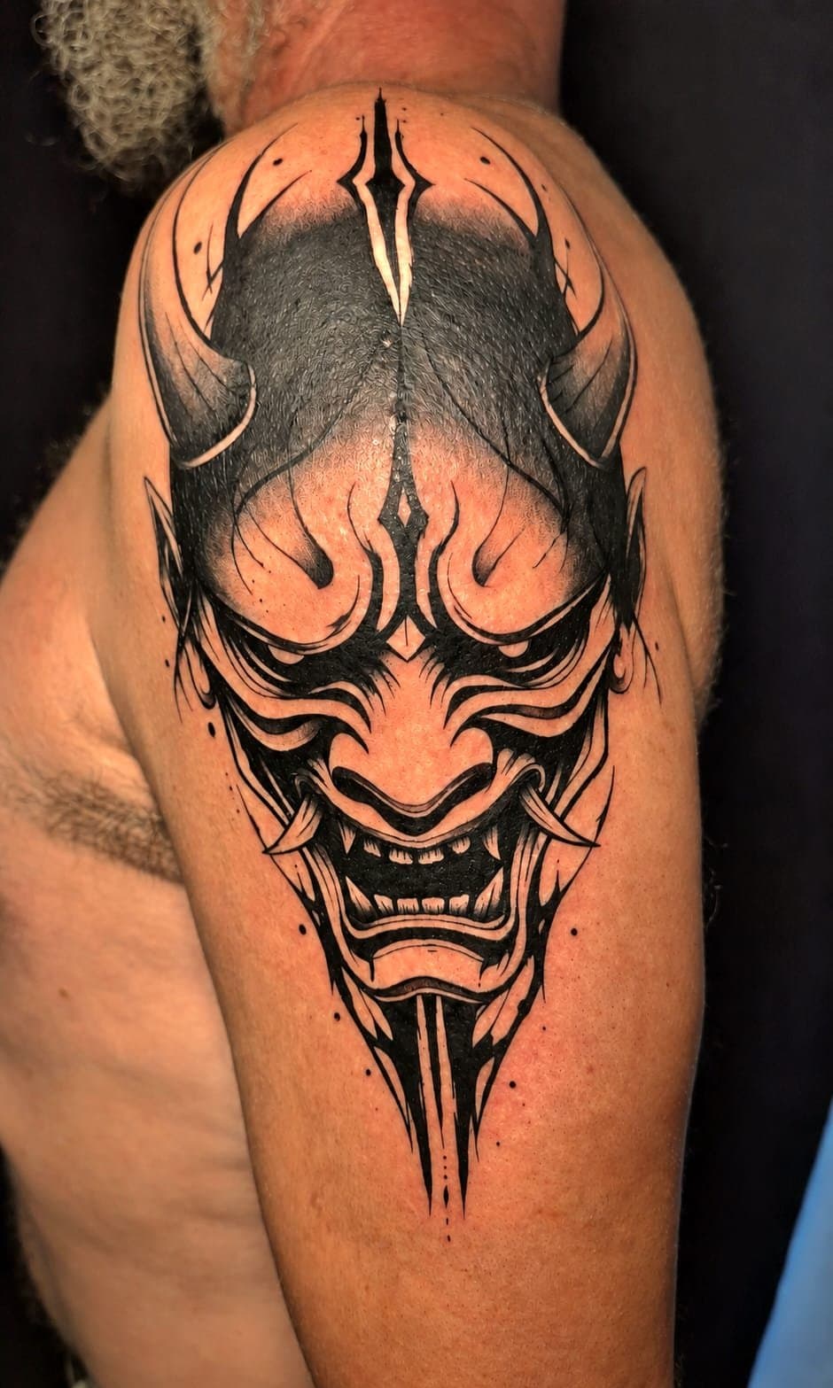 Masque hannya japonais aux cornes, tatoué en noir graphique sur l'épaule