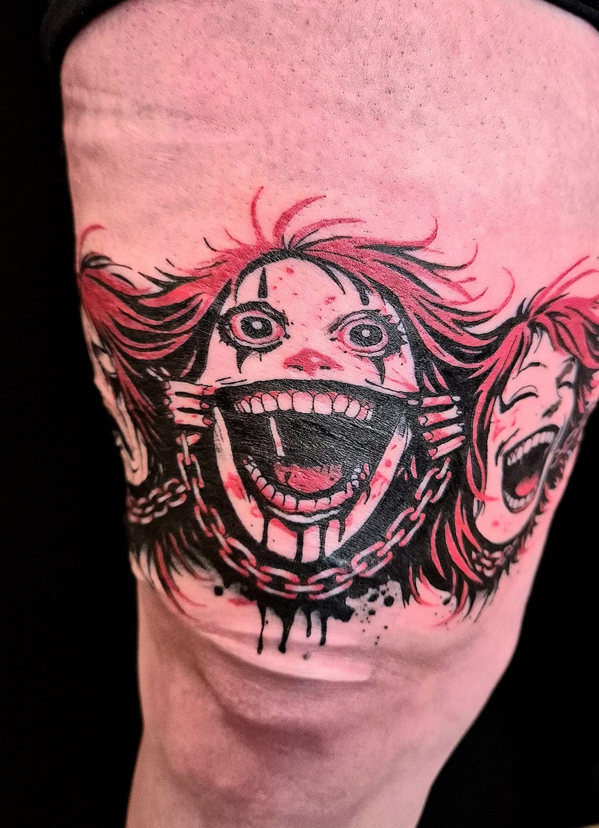 Tatouage manga, visages et chaînes en encre noire et rouge, sur la cuisse