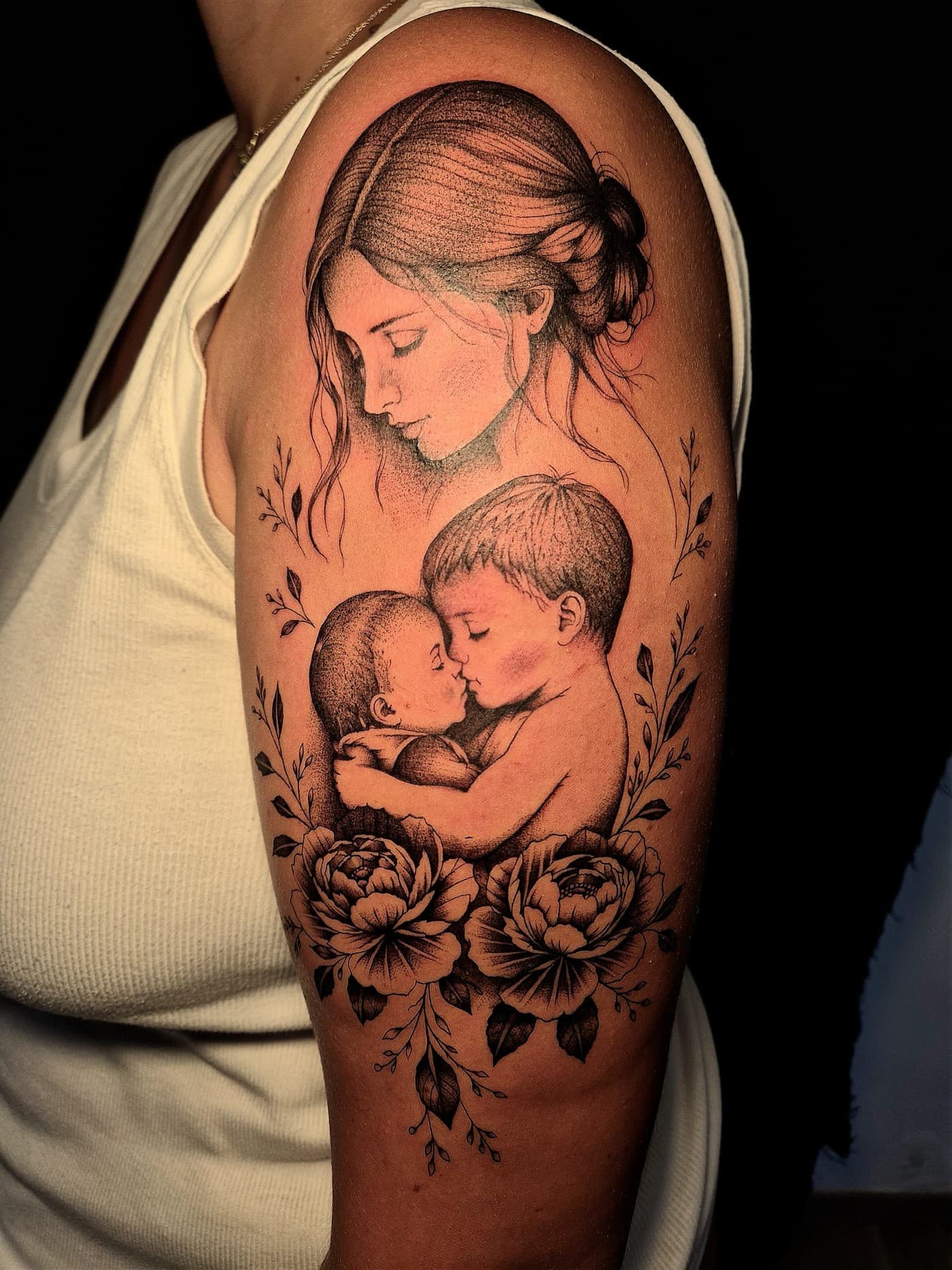 Mère et ses deux enfants entourés de pivoines, réalisme dotwork tatoué sur le bras