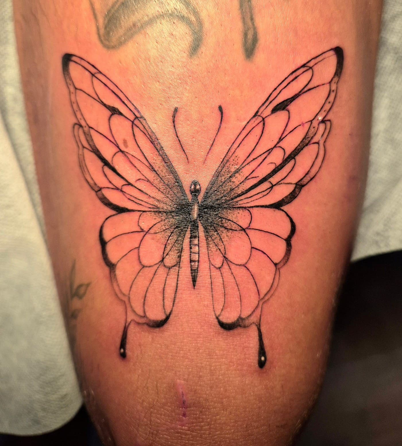 Papillon tatoué en ligne fine sur la cuisse, spécialité fine line du salon